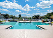 Thumbnail 14 of 38 - A large outdoor swimming pool surrounded by a concrete patio and a fence.