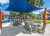 Thumbnail 31 of 38 - A patio with a table and chairs under a blue shade sail.
