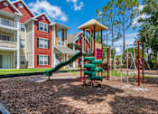 Thumbnail 29 of 38 - A playground with a green slide and red and white buildings in the background.