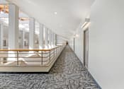 Thumbnail 8 of 35 - A long hallway with a carpeted floor and a railing on one side.