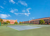 Thumbnail 24 of 35 - A tennis court is surrounded by a green fence and a brick building.