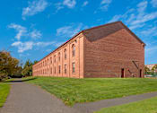 Thumbnail 31 of 35 - A long brick building with a pathway in front of it.