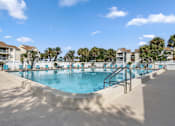 Thumbnail 15 of 30 - A large outdoor swimming pool surrounded by palm trees and lounge chairs.