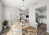 Thumbnail 1 of 30 - A dining room with a table set for two and a kitchen in the background.