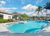 Thumbnail 4 of 32 - A large outdoor swimming pool with lounge chairs and an adjacent clubhouse overlooking a body of water