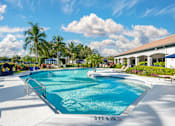 Thumbnail 3 of 32 - A large outdoor swimming pool with lounge chairs and an adjacent clubhouse overlooking a body of water