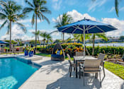 Thumbnail 6 of 32 - A poolside area with a table and chairs under an umbrella.