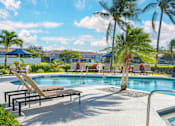 Thumbnail 5 of 32 - A large outdoor swimming pool with lounge chairs and an adjacent clubhouse overlooking a body of water