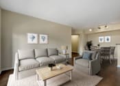 Thumbnail 17 of 32 - A living room with a grey sofa, a wooden coffee table, and a lamp.