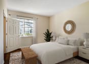 Thumbnail 15 of 32 - A bedroom with a white bed, a wooden bench, and a round mirror on the wall.