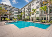 Thumbnail 16 of 49 - A swimming pool in front of a building with palm trees.