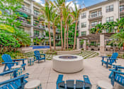 Thumbnail 23 of 49 - A patio with blue chairs and a fire pit in front of a building with balconies.