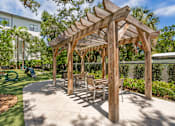 Thumbnail 43 of 49 - A wooden pergola with chairs and a table is in the middle of a sunny courtyard.