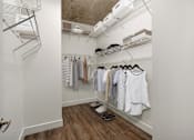 Thumbnail 5 of 48 - A walk in closet with clothes hanging on shelves and a pair of shoes on the floor.