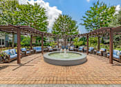 Thumbnail 18 of 49 - A fountain in the middle of a brick patio surrounded by trees and chairs.