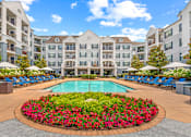 Thumbnail 10 of 49 - A large pool surrounded by a flower bed in front of apartment buildings.