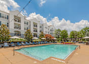 Thumbnail 11 of 49 - A large swimming pool in front of a white building with lounge chairs around it.