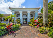 Thumbnail 20 of 33 - A white building with a blue trim and a red roof is surrounded by green plants.