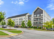 Thumbnail 39 of 42 - A modern apartment building with a curved driveway in front.