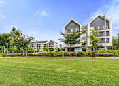 Thumbnail 36 of 42 - A large grassy area in front of a building with a bench.