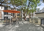 Thumbnail 25 of 38 - A wooden deck with a table and chairs and a red umbrella.