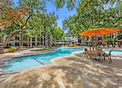 Thumbnail 12 of 38 - A pool surrounded by trees and chairs with an orange umbrella.