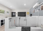 Thumbnail 32 of 38 - A bathroom with a white tiled shower area and a black door.