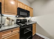 Thumbnail 6 of 38 - A kitchen with wooden cabinets and black appliances.