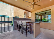 Thumbnail 19 of 29 - A patio with a bar and chairs under a ceiling fan.