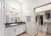 Thumbnail 9 of 29 - A bathroom with a sink, mirror, and a closet with clothes.