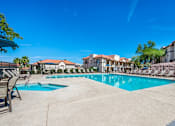 Thumbnail 16 of 37 - A large swimming pool surrounded by lounge chairs and buildings in the background.