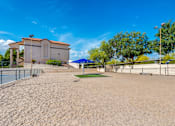 Thumbnail 26 of 37 - A sandy area with a building and trees in the background.