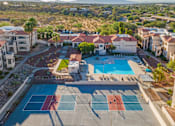 Thumbnail 32 of 37 - A tennis court is located in the middle of a courtyard with a pool and apartment buildings in the background.