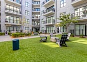 Thumbnail 16 of 27 - A modern apartment complex with a green lawn and outdoor furniture.