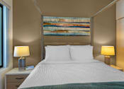 Thumbnail 9 of 27 - A bedroom with a large bed, two lamps, and a painting on the wall.