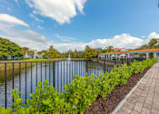 Thumbnail 14 of 28 - A walkway overlooking the water and a fountain with a metal railing and green landscape on the side.