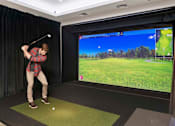 Thumbnail 33 of 39 - A man is playing golf in a room with a large screen showing a golf course.