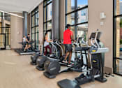Thumbnail 24 of 39 - A gym with people working out on treadmilers and elliptical machines.