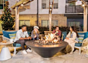 Thumbnail 22 of 39 - A group of people are sitting around a fire pit on a patio.
