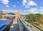 Thumbnail 24 of 34 - a rooftop patio with tables and umbrellas and a street with cars at The Merc, Waltham, 02453