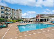 Thumbnail 22 of 29 - A large swimming pool surrounded by a patio area with lounge chairs and umbrellas.