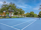 Thumbnail 25 of 41 - A blue tennis / pickleball court surrounded by trees l at Floresta apartments in Jupiter, FL