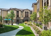 Thumbnail 7 of 36 - a sidewalk leading to an apartment building with lush green grass and trees at Estate at Woodmen Ridge, Colorado Springs, CO 80923