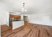 Thumbnail 3 of 50 - A room with wooden floors and a kitchen area with a refrigerator, microwave, and oven.