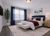 Thumbnail 12 of 20 - An apartment master bedroom with a large bed, a small table, and a potted plant.