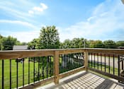 Thumbnail 12 of 16 - A wooden deck with a black railing and a view of a green lawn and trees.