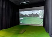 Thumbnail 14 of 21 - A golf simulator room with a screen showing a golf course.