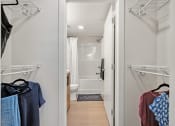 Thumbnail 9 of 21 - a walk in closet with clothes hanging on the wall and a bathroom in the background