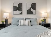 Thumbnail 8 of 21 - A bed with a grey comforter and striped pillows is flanked by two lamps on black nightstands.