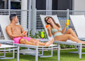 Thumbnail 25 of 27 - A man and a woman are sitting on lounge chairs outside, enjoying drinks and watermelon.at Icon One, Daytona Beach